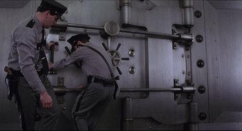 Movie still from “Quiz Show” (1994), directed by Robert Redford – A man in a police uniform climbing into a bank vault; Wide shot, Low angle