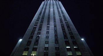 Movie still from “Quiz Show” (1994), directed by Robert Redford – A very tall building with many windows at night time; Extreme Wide shot, Low angle