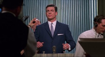 Movie still from “Quiz Show” (1994), directed by Robert Redford – A man wearing a suit and tie talking into microphones; Medium shot, Low angle