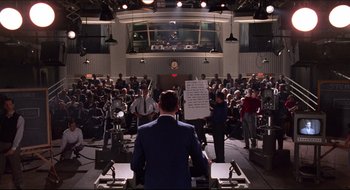 Movie still from “Quiz Show” (1994), directed by Robert Redford – A group of people standing around a room; Extreme Wide shot, High angle