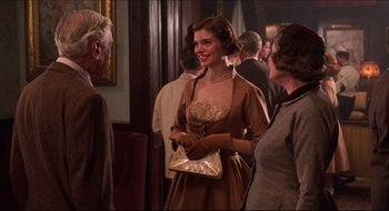 Movie still from “Quiz Show” (1994), directed by Robert Redford – A woman in a brown dress talking to some people; Medium shot, Over the shoulder angle