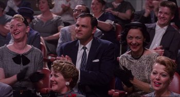 Movie still from “Quiz Show” (1994), directed by Robert Redford – A group of people sitting in a theater clapping; Medium shot, Low angle