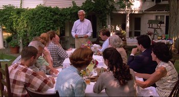 Movie still from “Quiz Show” (1994), directed by Robert Redford – An older man standing in front of a group of people at a table; Wide shot, Over the shoulder angle