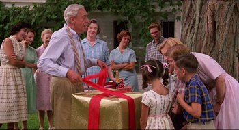 Movie still from “Quiz Show” (1994), directed by Robert Redford – An older man cutting a red ribbon with a group of people around him; Medium shot, High angle