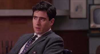 Movie still from “Quiz Show” (1994), directed by Robert Redford – A man in a suit and tie sitting in a chair; Close Up shot, Over the shoulder angle