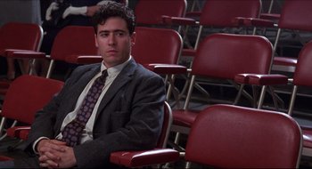Movie still from “Quiz Show” (1994), directed by Robert Redford – A man in a suit and tie sitting in a red chair; Medium shot, Low angle