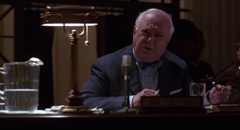 Movie still from “Quiz Show” (1994), directed by Robert Redford – An older man sitting at a desk in front of a microphone; Medium shot, High angle