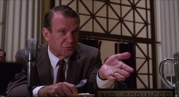 Movie still from “Quiz Show” (1994), directed by Robert Redford – A man in a suit and tie sitting at a table; Close Up shot, Over the shoulder angle