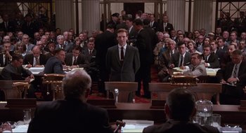 Movie still from “Quiz Show” (1994), directed by Robert Redford – A man in a suit stands in front of an audience; Wide shot, High angle