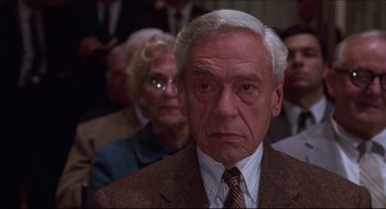 Movie still from “Quiz Show” (1994), directed by Robert Redford – An older man wearing a suit and tie in front of a group of people; Close Up shot, Low angle