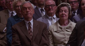 Movie still from “Quiz Show” (1994), directed by Robert Redford – An older man and woman are sitting in a crowd; Medium shot, Low angle
