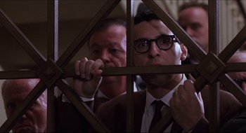 Movie still from “Quiz Show” (1994), directed by Robert Redford – A man in a suit and tie looking through a window; Medium shot, Low angle