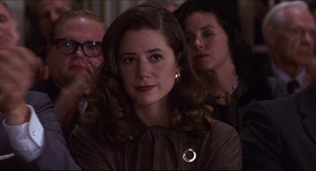 Movie still from “Quiz Show” (1994), directed by Robert Redford – A young woman with long brown hair wearing a brown jacket; Close Up shot, Over the shoulder angle