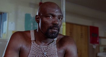 Movie still from “Raising Arizona” (1987), directed by Joel Coen – A bald man with a beard and a necklace; Close Up shot, Low angle