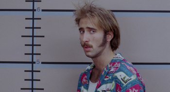 Movie still from “Raising Arizona” (1987), directed by Joel Coen – A man with a beard and mustache standing in front of a wall; Close Up shot, Low angle