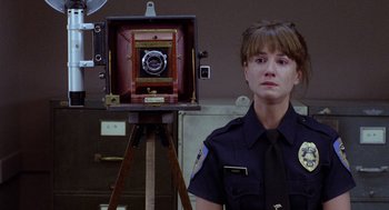 Movie still from “Raising Arizona” (1987), directed by Joel Coen – A police officer standing in front of an old camera; Close Up shot, Low angle