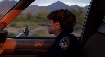 Movie still from “Raising Arizona” (1987), directed by Joel Coen – A police officer sitting in the back seat of a car; Close Up shot, Over the shoulder angle