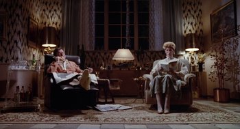 Movie still from “Raising Arizona” (1987), directed by Joel Coen – A man and a woman sitting in a living room reading; Wide shot, High angle