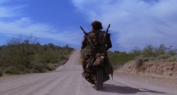 Movie still from “Raising Arizona” (1987), directed by Joel Coen – A man riding a motorcycle down the middle of a dirt road; Wide shot, Low angle