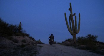 Movie still from “Raising Arizona” (1987), directed by Joel Coen – A person riding a motorcycle down a dirt road at night; Wide shot, Low angle
