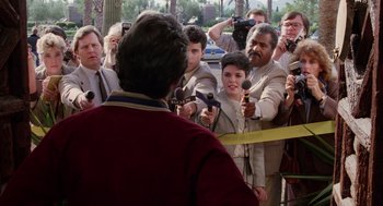 Movie still from “Raising Arizona” (1987), directed by Joel Coen – A group of people standing next to each other holding microphones; Medium shot, Over the shoulder angle