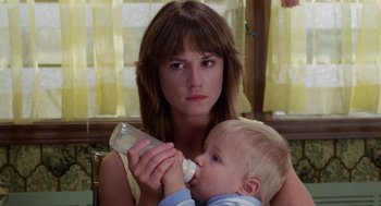 Movie still from “Raising Arizona” (1987), directed by Joel Coen – A woman holding a baby while holding a bottle in her hand; Close Up shot, Low angle