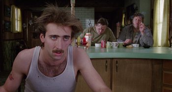 Movie still from “Raising Arizona” (1987), directed by Joel Coen – A man sitting in front of a counter with two other men sitting in the background; Close Up shot, Low angle