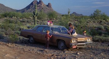 Movie still from “Raising Arizona” (1987), directed by Joel Coen – A group of people sitting on the hood of an old car; Wide shot, High angle