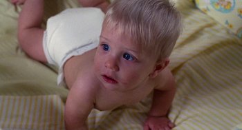 Movie still from “Raising Arizona” (1987), directed by Joel Coen – A baby is sitting on a bed and looking up at the camera; Close Up shot, High angle