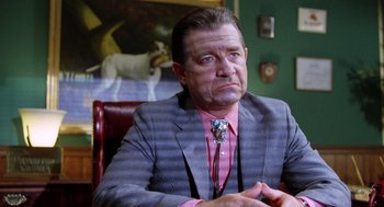 Movie still from “Raising Arizona” (1987), directed by Joel Coen – A person sitting in a chair wearing a suit; Close Up shot, Low angle