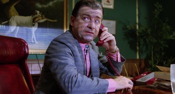 Movie still from “Raising Arizona” (1987), directed by Joel Coen – A man talking on a phone while sitting in a chair; Medium shot, Low angle