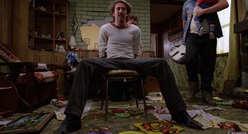 Movie still from “Raising Arizona” (1987), directed by Joel Coen – A man sitting on a chair in the middle of a room; Medium shot, Low angle