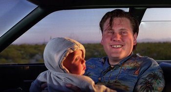 Movie still from “Raising Arizona” (1987), directed by Joel Coen – A man holding a baby in his arms in a car; Close Up shot, Low angle