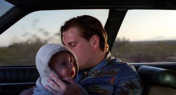 Movie still from “Raising Arizona” (1987), directed by Joel Coen – A man holding a baby in his arms while sitting in a car; Close Up shot, Low angle