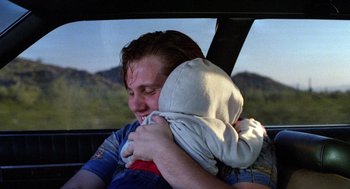 Movie still from “Raising Arizona” (1987), directed by Joel Coen – A man holding a baby in his arms in a car; Close Up shot, Over the shoulder angle