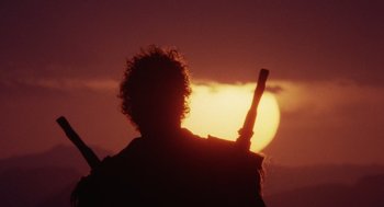 Movie still from “Raising Arizona” (1987), directed by Joel Coen – A person holding a baseball bat in front of a sunset; Wide shot, Low angle
