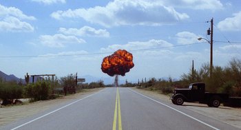 Movie still from “Raising Arizona” (1987), directed by Joel Coen – A car driving down a road with a large explosion in the background; Extreme Wide shot, Low angle