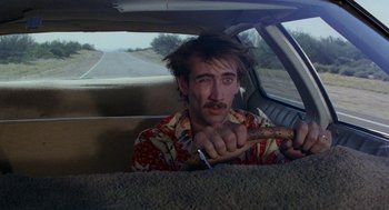 Movie still from “Raising Arizona” (1987), directed by Joel Coen – A man sitting in the back seat of a car holding a hot dog; Close Up shot, Over the shoulder angle