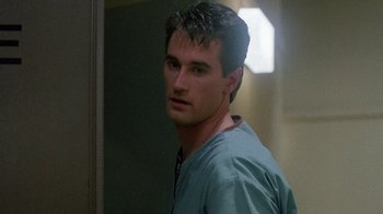 Movie still from “Re-Animator” (1985), directed by Stuart Gordon – A man in a hospital gown standing in front of a door; Close Up shot, Low angle