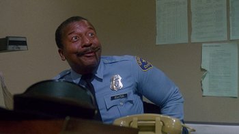 Movie still from “Re-Animator” (1985), directed by Stuart Gordon – A police officer sitting in front of a microphone; Close Up shot, Low angle