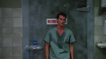 Movie still from “Re-Animator” (1985), directed by Stuart Gordon – A man standing in front of a restroom door; Medium shot, Low angle