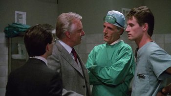 Movie still from “Re-Animator” (1985), directed by Stuart Gordon – A group of men standing next to each other in a room; Medium shot, Over the shoulder angle
