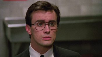 Movie still from “Re-Animator” (1985), directed by Stuart Gordon – A person wearing a suit and glasses; Close Up shot, Low angle