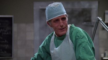 Movie still from “Re-Animator” (1985), directed by Stuart Gordon – A man wearing a surgical gown and a hat; Close Up shot, Low angle