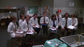 Movie still from “Re-Animator” (1985), directed by Stuart Gordon – A group of people in white lab coats sitting in a room; Wide shot, High angle