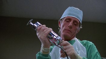 Movie still from “Re-Animator” (1985), directed by Stuart Gordon – A man in a surgeon's outfit is holding an instrument in his hands; Close Up shot, Low angle