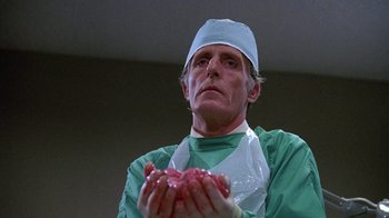 Movie still from “Re-Animator” (1985), directed by Stuart Gordon – A man in a surgical gown holding a piece of meat; Close Up shot, Low angle