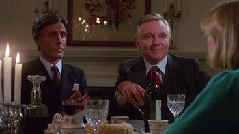 Movie still from “Re-Animator” (1985), directed by Stuart Gordon – Two men sitting at a table with a bottle of wine; Medium shot, Over the shoulder angle