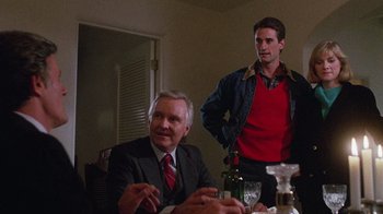 Movie still from “Re-Animator” (1985), directed by Stuart Gordon – A man standing next to a man sitting at a dinner table; Medium shot, Over the shoulder angle