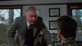 Movie still from “Re-Animator” (1985), directed by Stuart Gordon – An older man wearing a suit talking to a young man; Medium shot, Over the shoulder angle